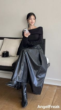 Woman in a black off-shoulder top and long black skirt sitting indoors