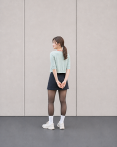 Woman with a ponytail wearing a short skirt and black tights, looking over her shoulder
