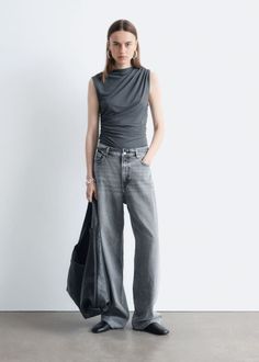 Woman in a gray sleeveless top and wide leg jeans holding a black bag