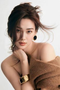 Woman with brown hair and gold jewelry wearing a brown sweater off the shoulders
