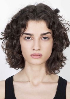 Woman with short curly dark hair wearing a black tank top against a white background