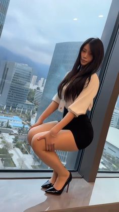 Woman in a black skirt and high heels posing by a window overlooking a cityscape