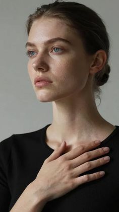Woman with blue eyes and a black shirt, hand on chest