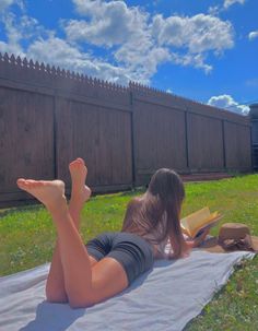 Woman lying on a blanket in a yard reading a book on a sunny day