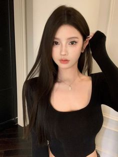 Woman with long dark hair wearing a black top and necklace indoors