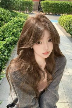 Woman with long brown hair wearing a gray cardigan outdoors