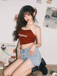 Woman with long hair wearing a red crop top and denim shorts, kneeling indoors