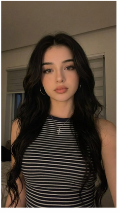 Woman with long black hair wearing a striped top and cross necklace indoors