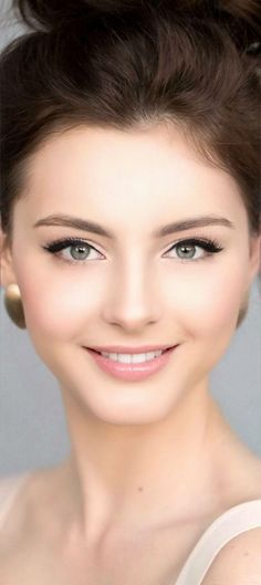 Woman with brown hair in an updo, smiling with green eyes and gold earrings