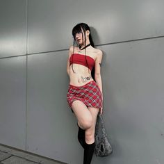 Woman in a red tube top and plaid mini skirt leaning against a wall