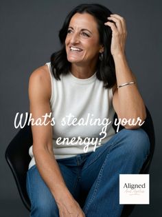 Woman with dark hair wearing a white sleeveless top and blue jeans, smiling in a studio