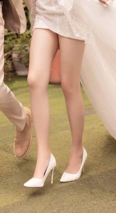 Woman in a short wedding dress and white heels with a man's leg nearby