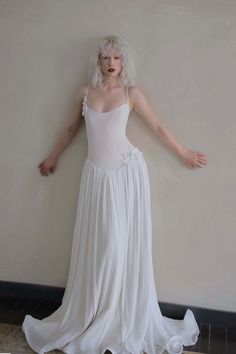 Woman with curly blonde hair in a white dress leaning against a wall