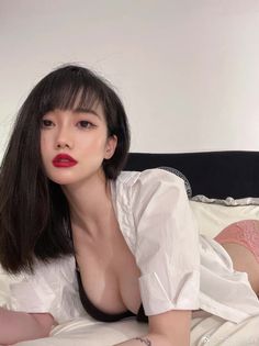 Woman with black hair and red lipstick in a white shirt and pink underwear on a bed