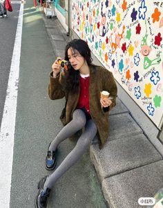 Woman with long hair holding a camera and ice cream on a street with a colorful mural