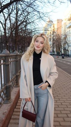 Woman with blonde hair wearing a light coat and jeans on a street