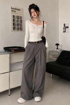 Woman in a white long sleeve top and grey wide leg pants indoors