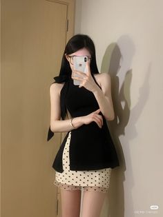 Woman in a black halter top and polka dot skirt taking a mirror selfie