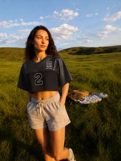 Woman in a crop top and shorts standing in a green field at golden hour