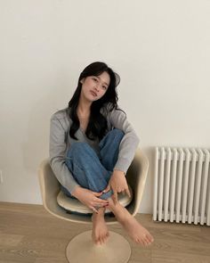 Woman with long dark hair sitting in a chair, wearing jeans and a gray cardigan