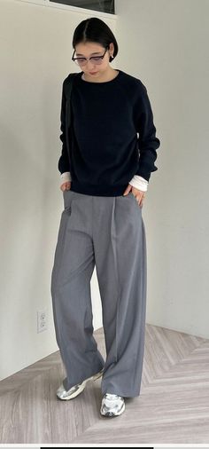 Woman with short hair and glasses wearing a black sweater and wide leg pants indoors