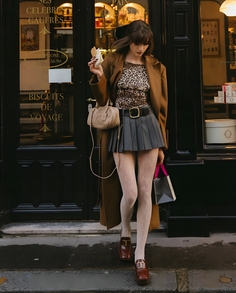 Woman in a long coat and pleated skirt holding a shopping bag on a street