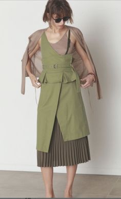 Woman in a green dress with a pleated skirt and cardigan, wearing sunglasses indoors