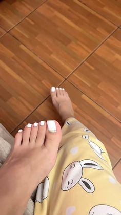 Feet with white toenails and bunny print pants on a wooden floor