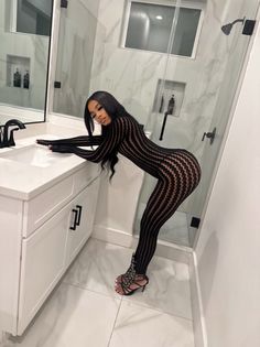Woman in a black patterned jumpsuit and high heels posing in a bathroom