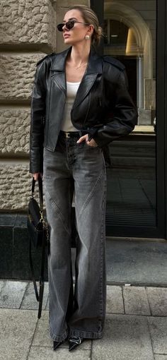 Woman in a black leather jacket and wide leg jeans holding a black handbag