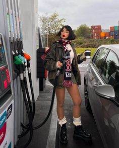 Woman in a leather jacket and scarf holding a gas pump and coffee cup