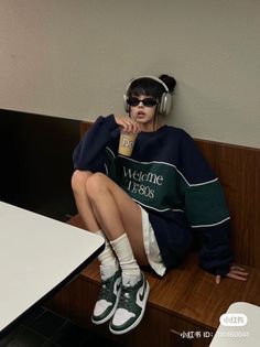 Person in an oversized sweatshirt, sunglasses, and headphones sitting indoors