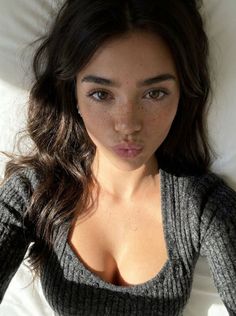 Woman with long dark hair and freckles wearing a grey top, making a pouty face