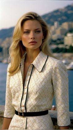 Blonde woman in a patterned shirt with a black belt outdoors with a cityscape background