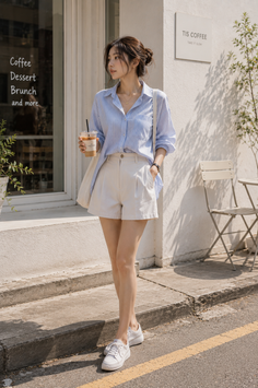Woman in a striped shirt and white shorts holding iced coffee on a sunny street