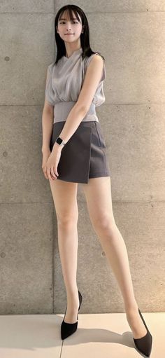 Woman with black hair wearing a short skirt and high heels against a concrete wall