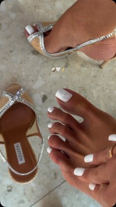 Feet with white pedicure and sparkling high heels on a marble floor