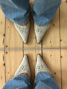Person wearing blue jeans and pointed shoes with cut-out details, reflected in a mirror