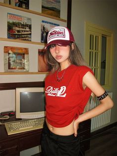 Woman in a red crop top and trucker hat posing indoors