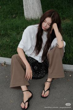 Woman with long hair wearing a white t-shirt and brown pants, sitting outdoors