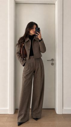 Woman in a brown suit and black turtleneck taking a mirror selfie