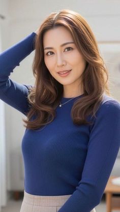 Woman with long brown hair wearing a blue ribbed top and silver necklace