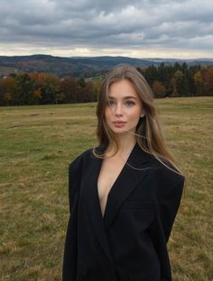 Woman in a black blazer with exposed skin standing in a field with autumn trees