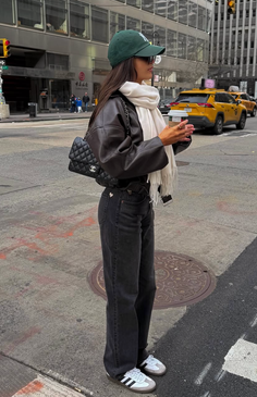 Woman in a baseball cap, leather jacket, and jeans on a city street