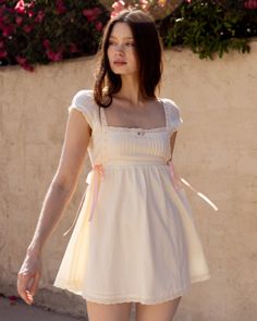 Woman in a white dress with pink ribbons and lace trim outdoors