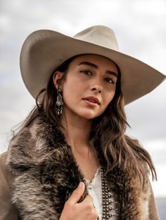 Woman in a cowboy hat and fur collar with silver earrings outdoors