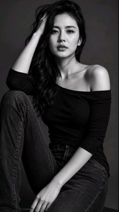 Woman with long hair wearing an off-shoulder top and jeans in a black and white portrait