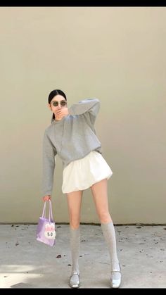 Woman in a grey sweatshirt and white skirt holding a purple bag outdoors