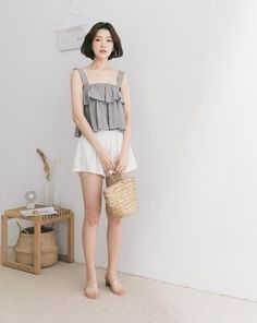 Woman with short hair wearing a ruffle top and white shorts, holding a straw bag
