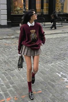 Woman in a plaid skirt and teddy bear sweater walking on a cobblestone street